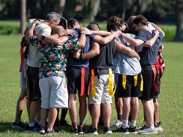 group of men playin flag football, praying together